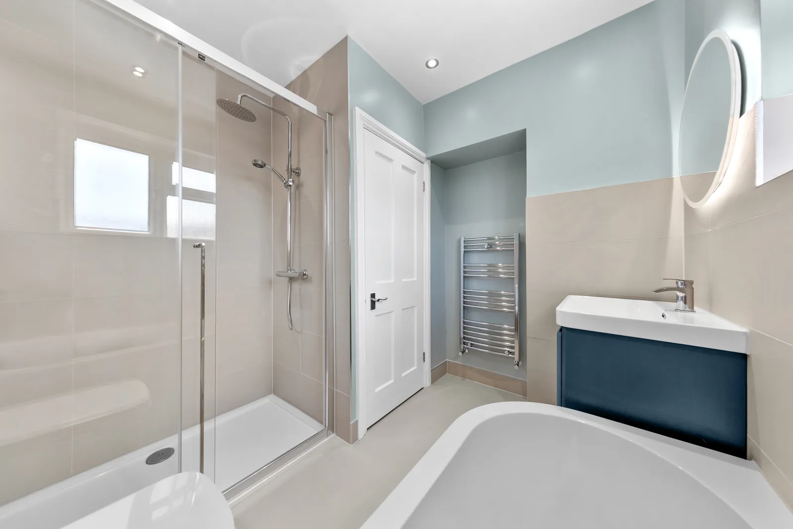Full bathroom renovation with navy fitted vanity unit and round LED backlit mirror completed in Orpington, BR6 by Buildaway